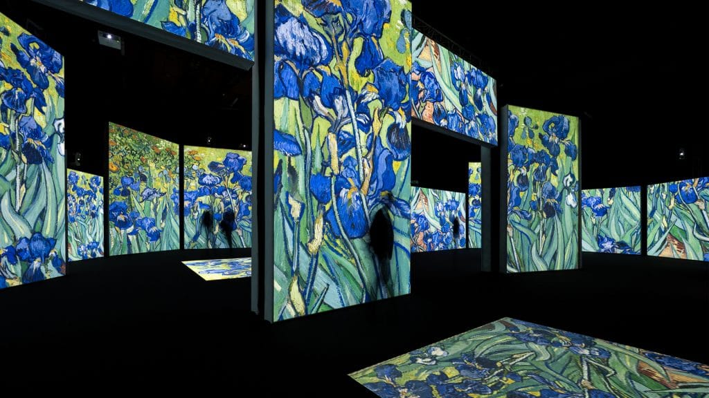 A dark room with multiple screens showing projections of Vincent Van Gogh's Irises painting