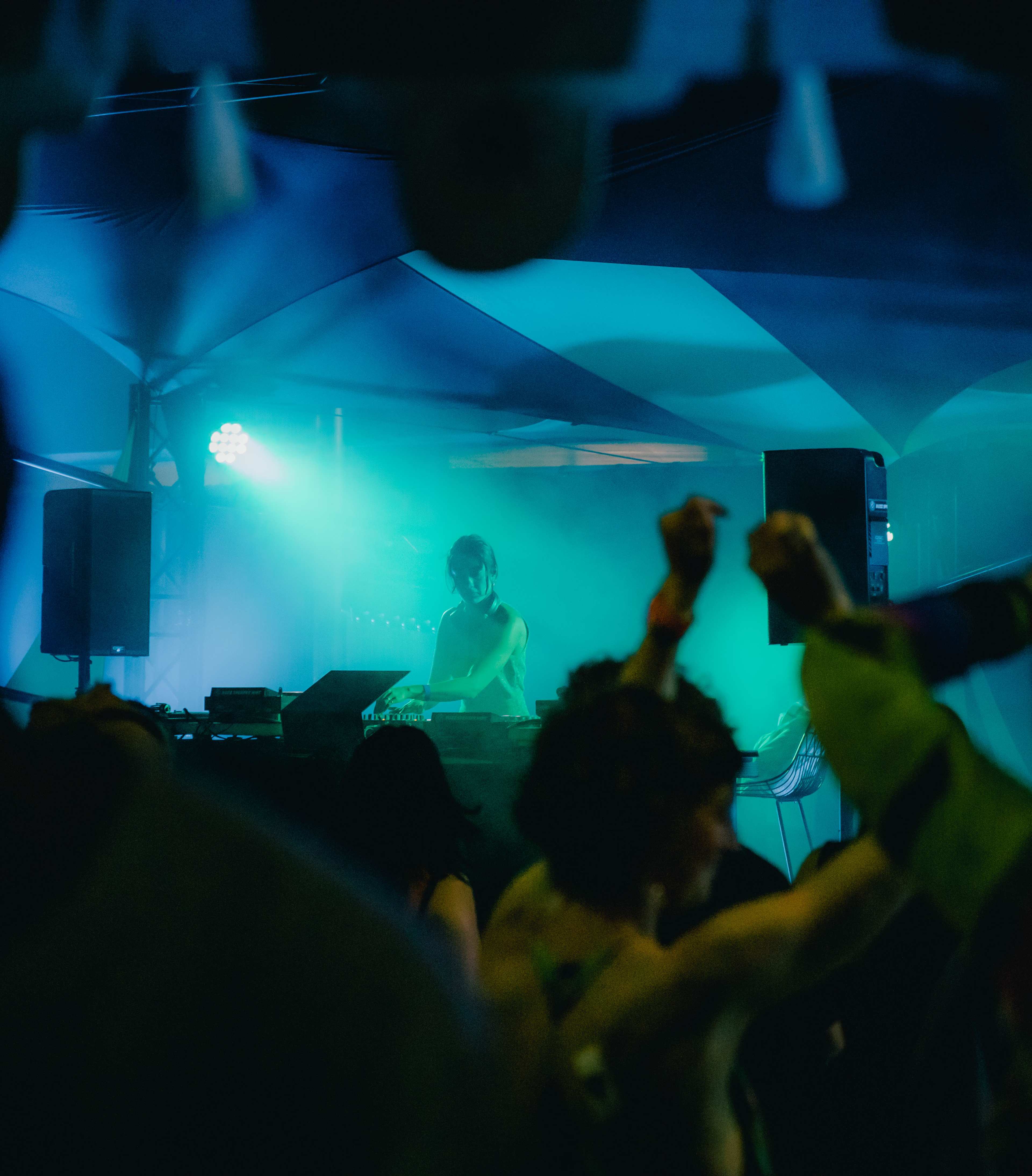 Image of a busy crowd dancing to a DJ, performing in front of blue light